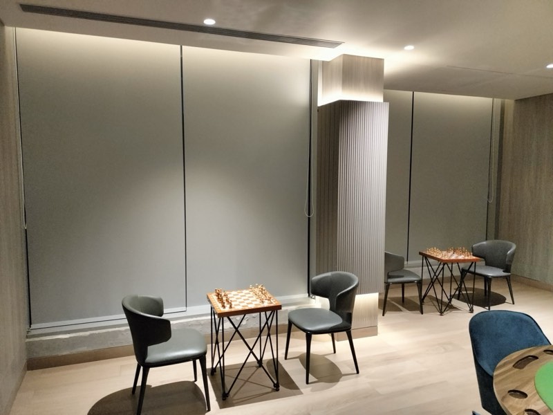 Grey dim-out roller blinds in a lounge with chess tables